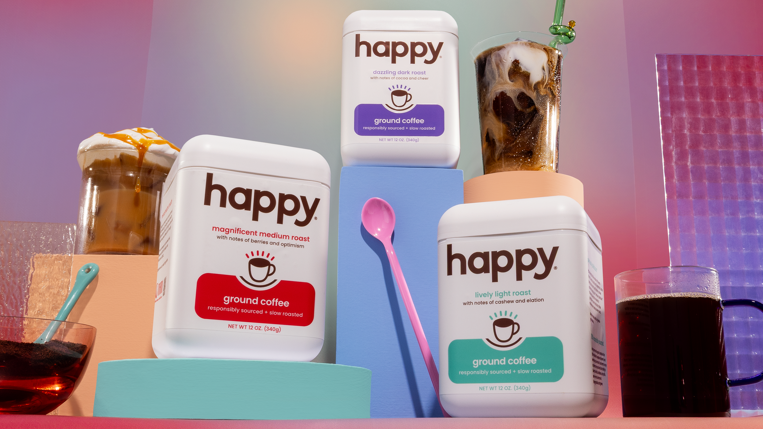Three 'happy' branded coffee packages with a cup of coffee and a glass of coffee on a colorful background.