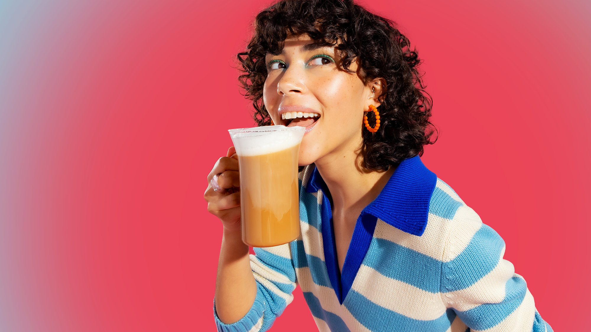 Woman drinking from a cup against a pink background