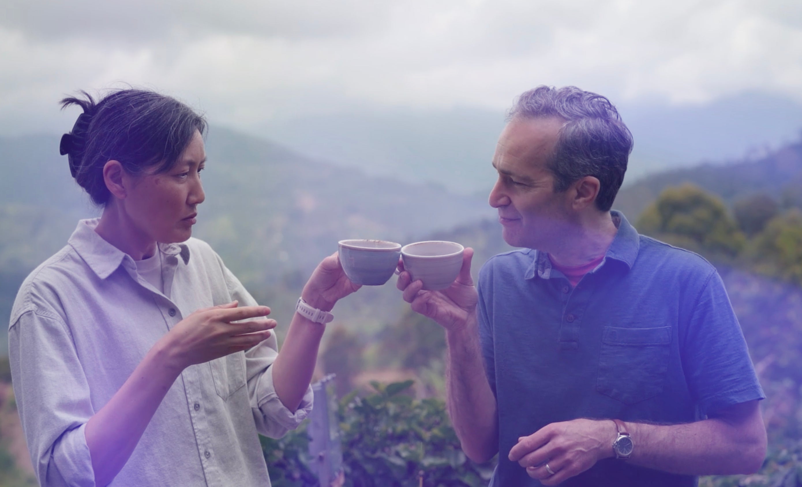Two Coffee Q-Graders holding tea cups in a scenic outdoor setting with mountains.