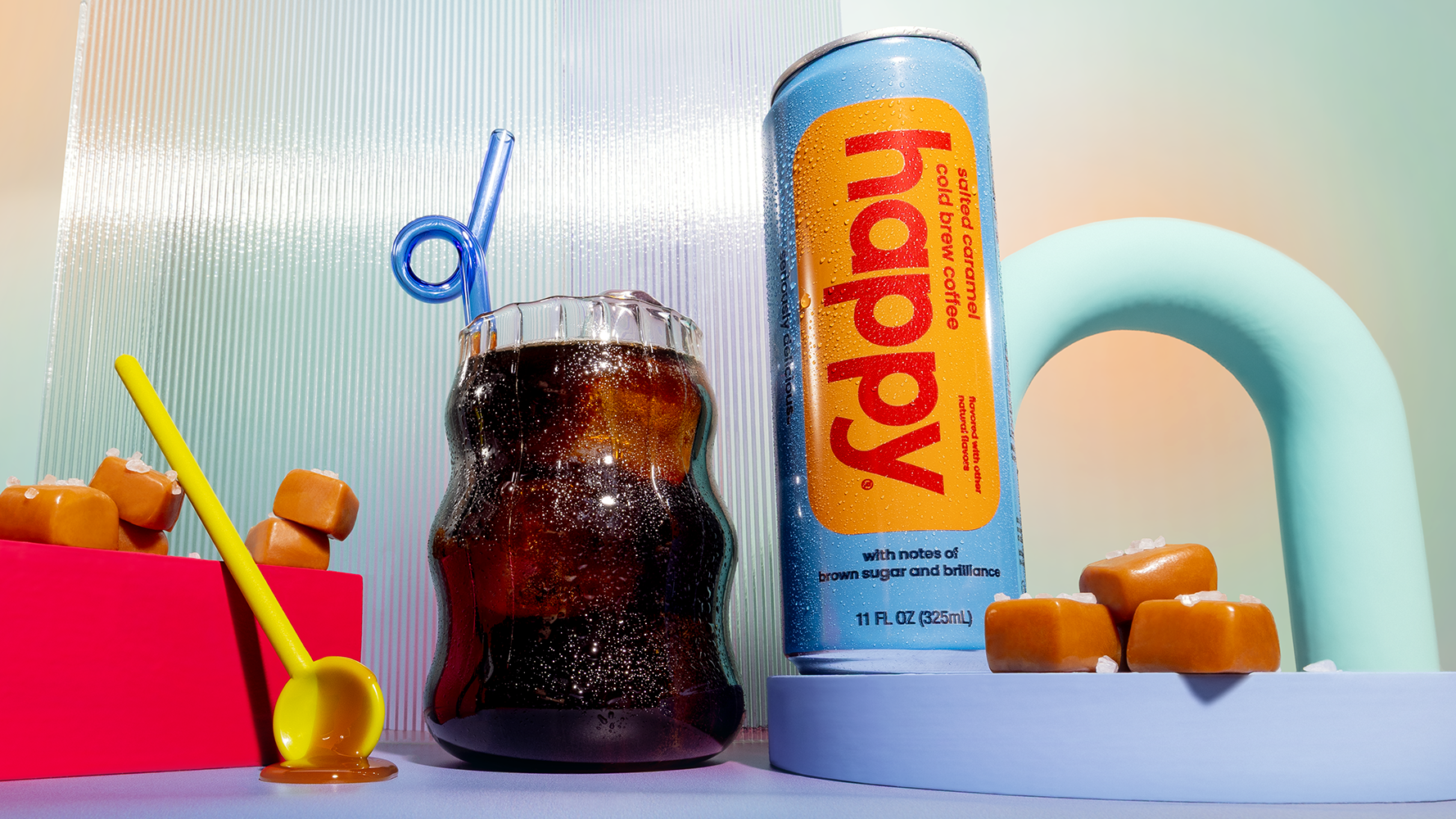 Can of 'happy' Salted Caramel Cold Brew with a glass of Cold brew coffee and caramels on a colorful background