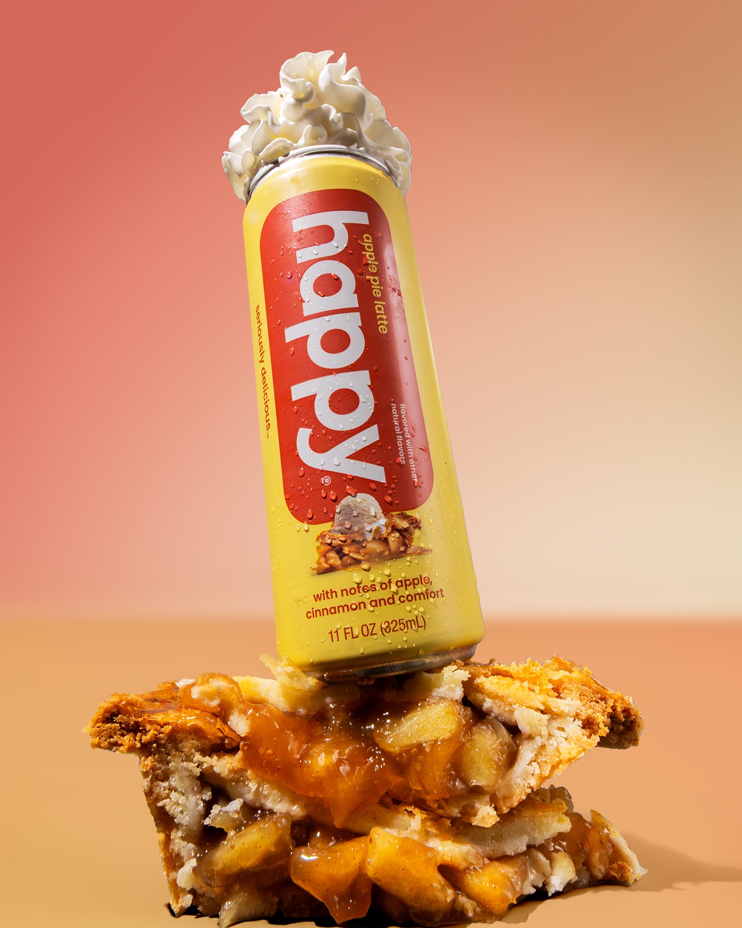Can of 'happy' apple pie latte on top of a slice of apple pie with a gradient background and whipped cream on top