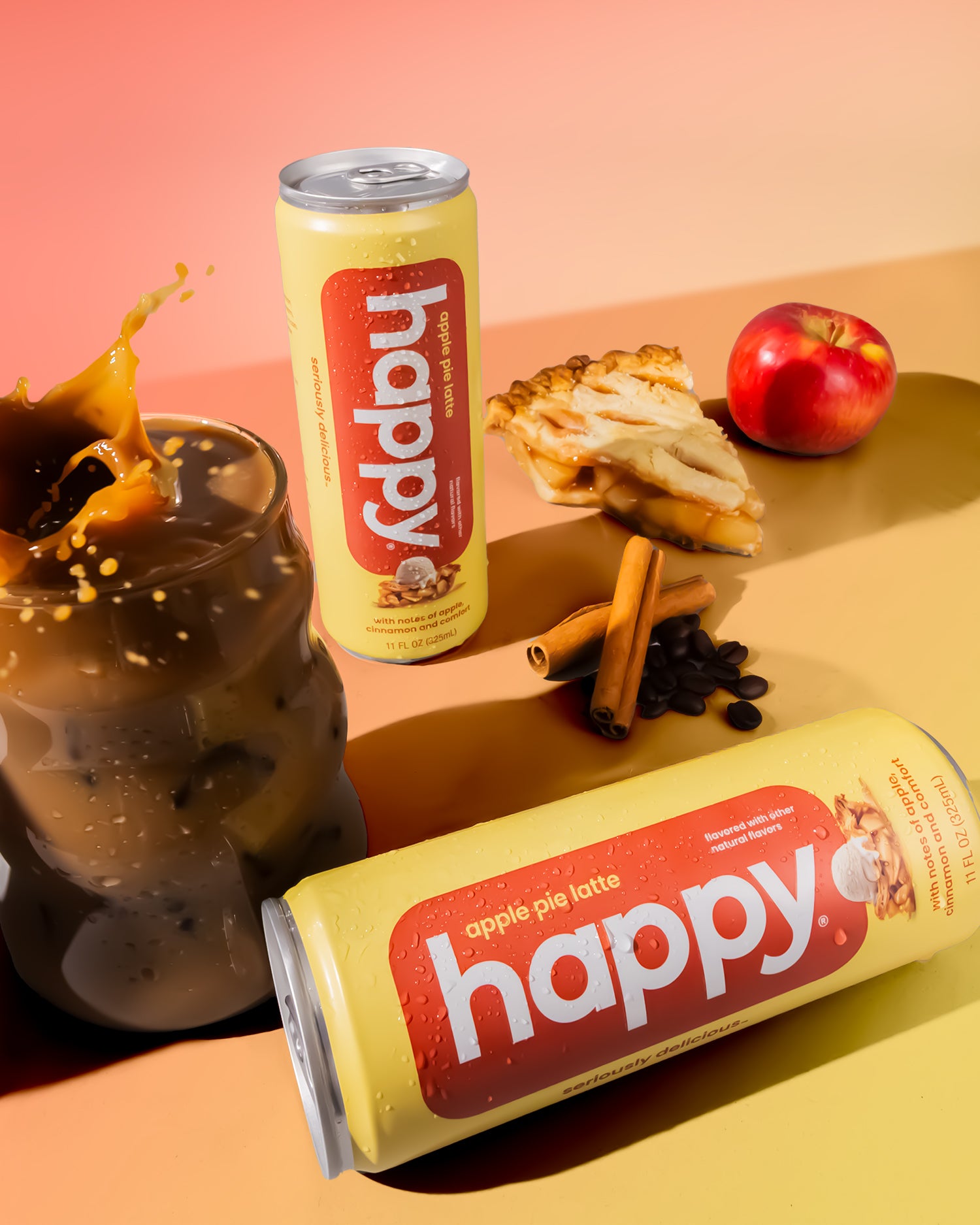Two cans of 'happy' apple pie latte on a colorful background with coffee and apples.