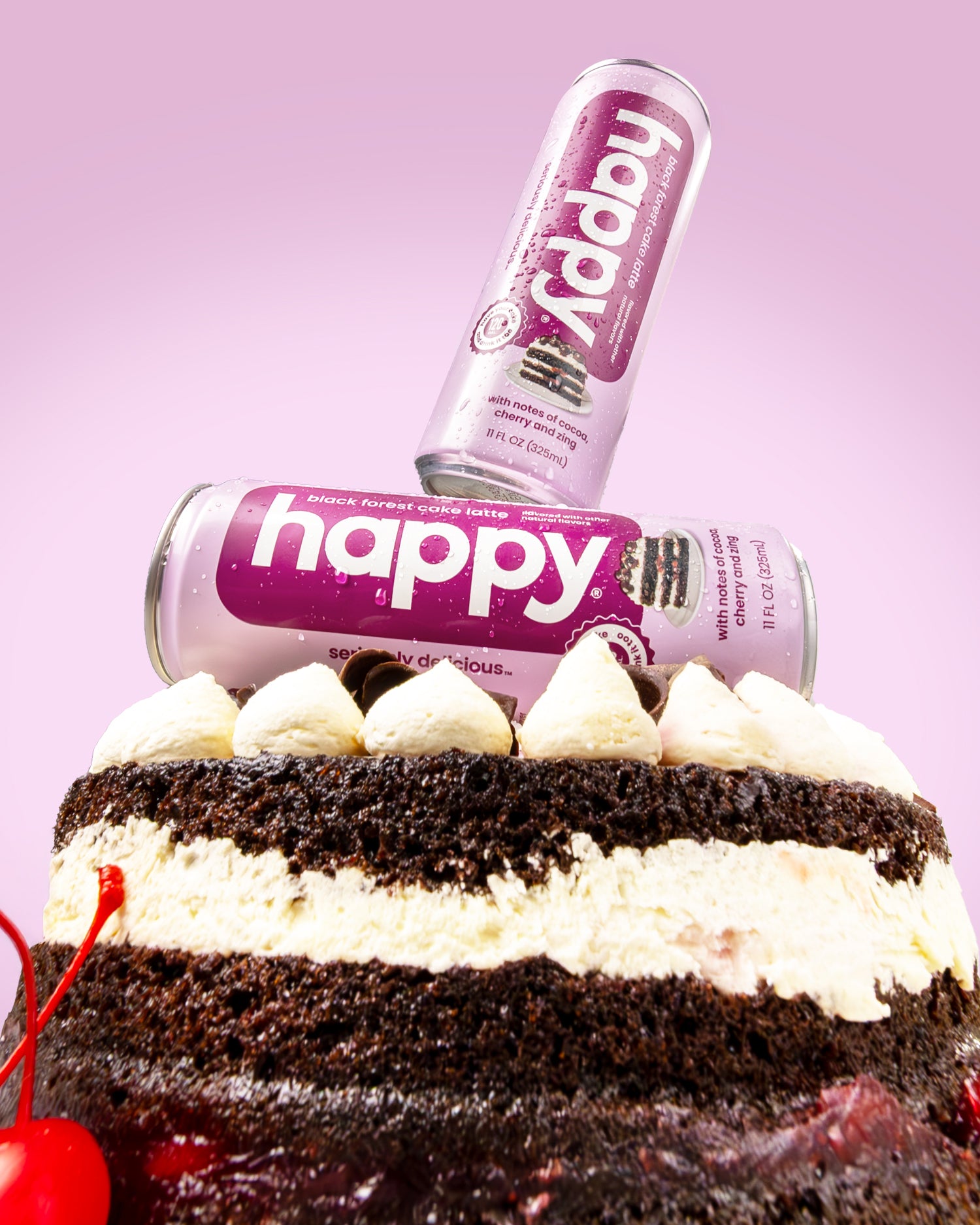 Two cans of Happy Black Forest Cake Latte on top of a chocolate cake with whipped cream.