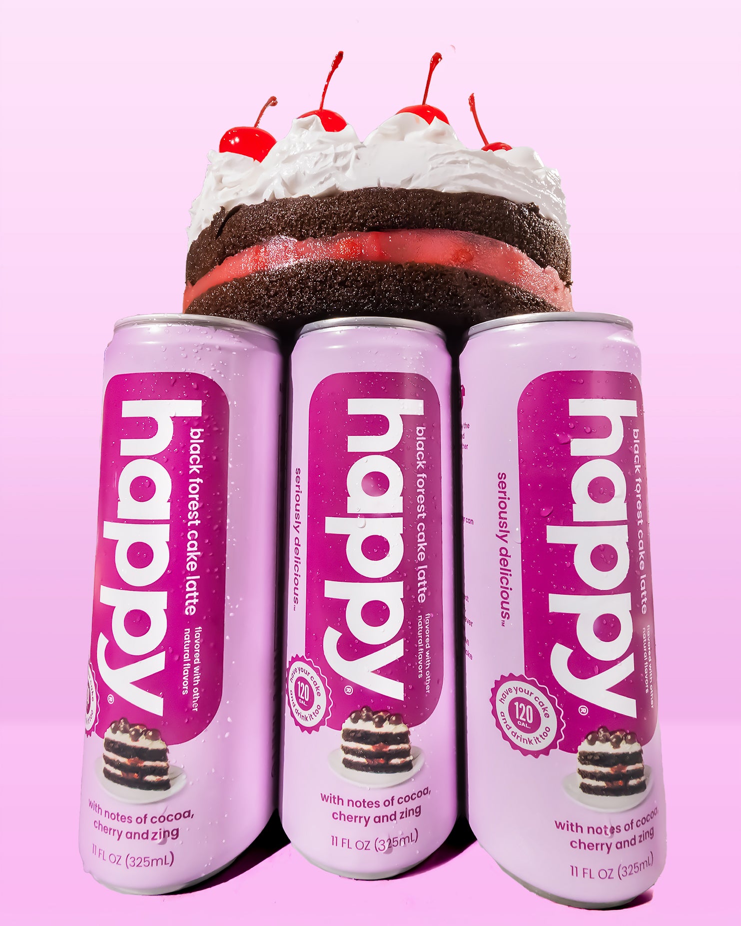 Three cans of 'happy' Black Forest cake latte with a cake and cherries on top against a pink background.