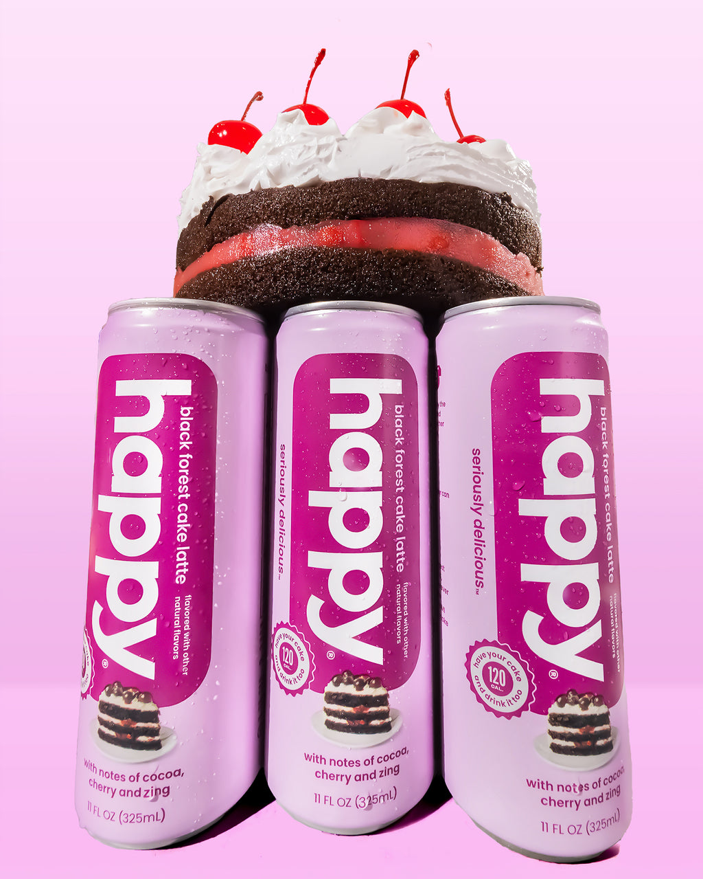 Three cans of 'happy' Black Forest cake latte with a cake and cherries on top against a pink background.