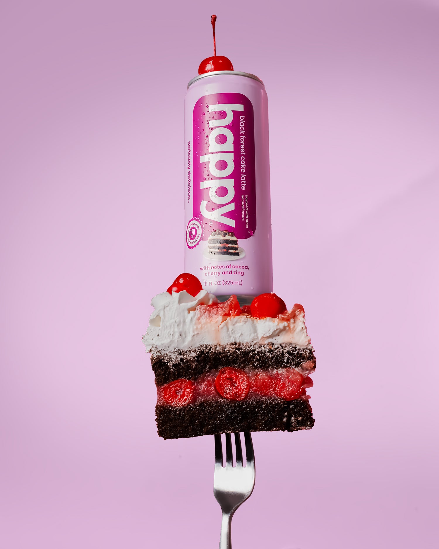 Pink can of Happy Black Forest Cake Latte sitting on top of piece of chocolate cake with whipped cream resting on a fork.  
