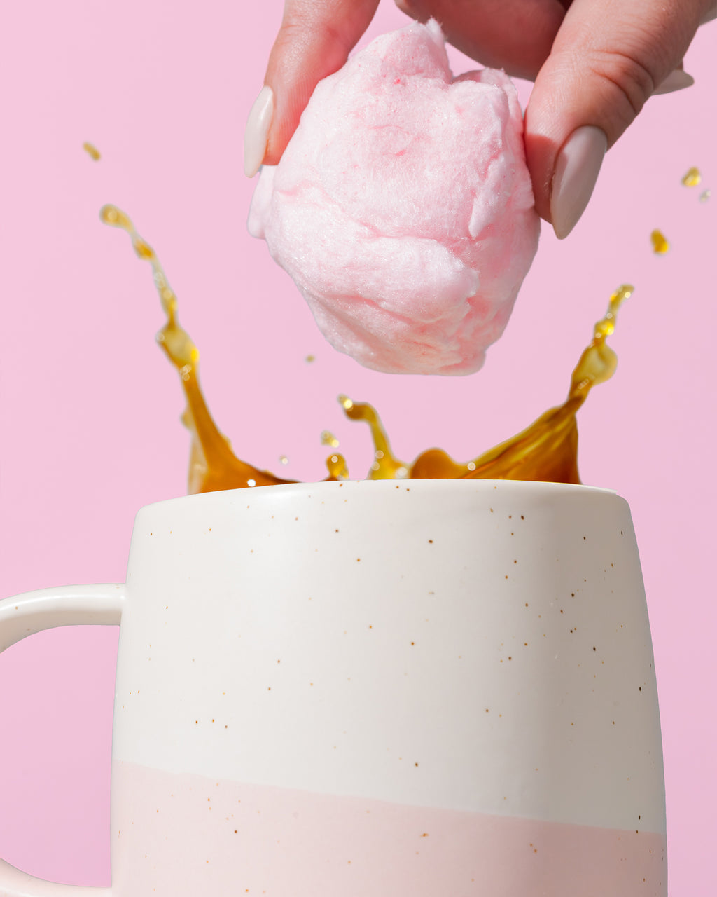 Pink cotton candy being dropped into a white mug of coffee against a pink background