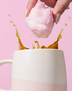 Pink cotton candy being dropped into a white mug of coffee against a pink background