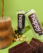 Two cans of happy dubai chocolatey style latte with a glass of iced coffee, pistachios, and dubai chocolate bars on a green background.