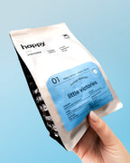 Hand holding a 'little victories' speciality Nicaraguan coffee package against a light blue background