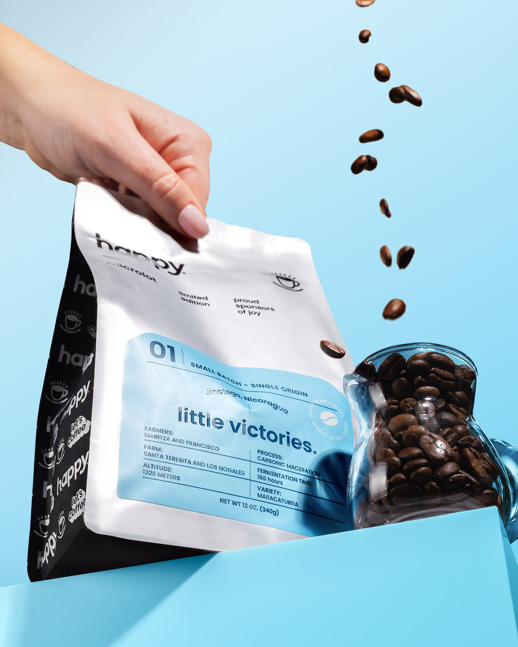 Hand opening a small batch coffee bag of 'happy' microlot with high quality coffee beans spilling out on a blue background