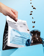 Hand opening a small batch coffee bag of 'happy' microlot with high quality coffee beans spilling out on a blue background