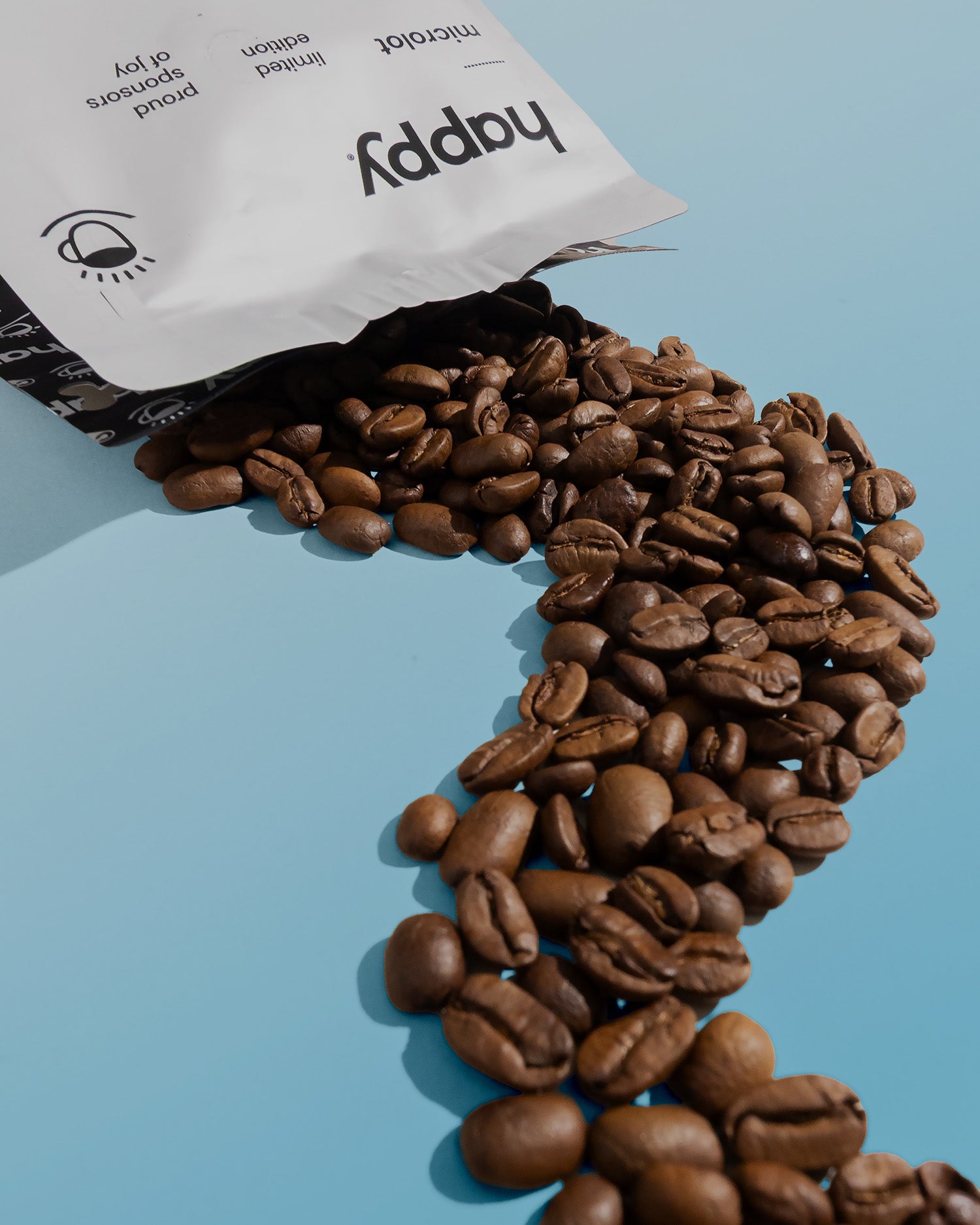 Coffee beans spilling out of a 'happy' branded bag on a light blue background