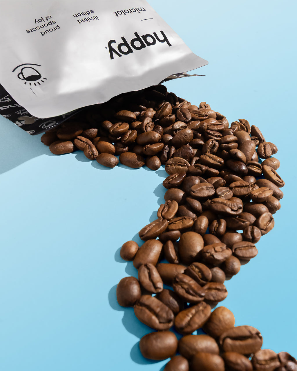 Coffee beans spilling out of a 'happy' speciality grade coffee microlot bag on a light blue background