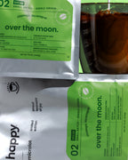 Over the Moon Decaf Coffee bag on its side with coffee, from happy on a green background