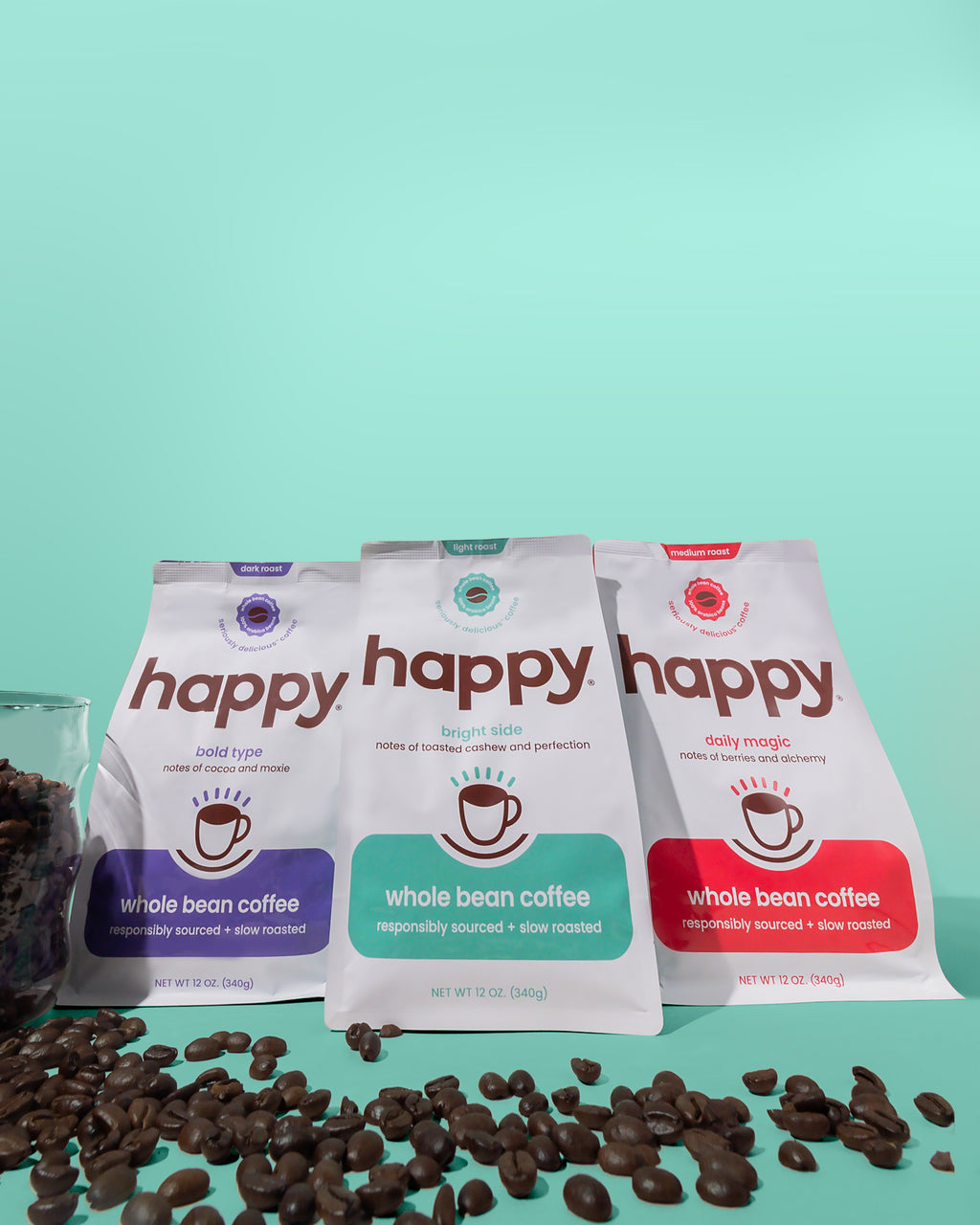 Three 'happy' brand whole bean coffee packages with scattered coffee beans on a teal background