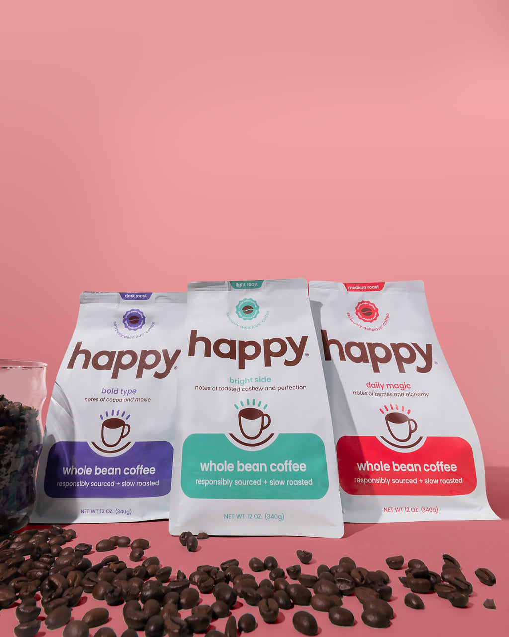 Three 'happy' brand whole bean coffee packages with scattered coffee beans on a pink background