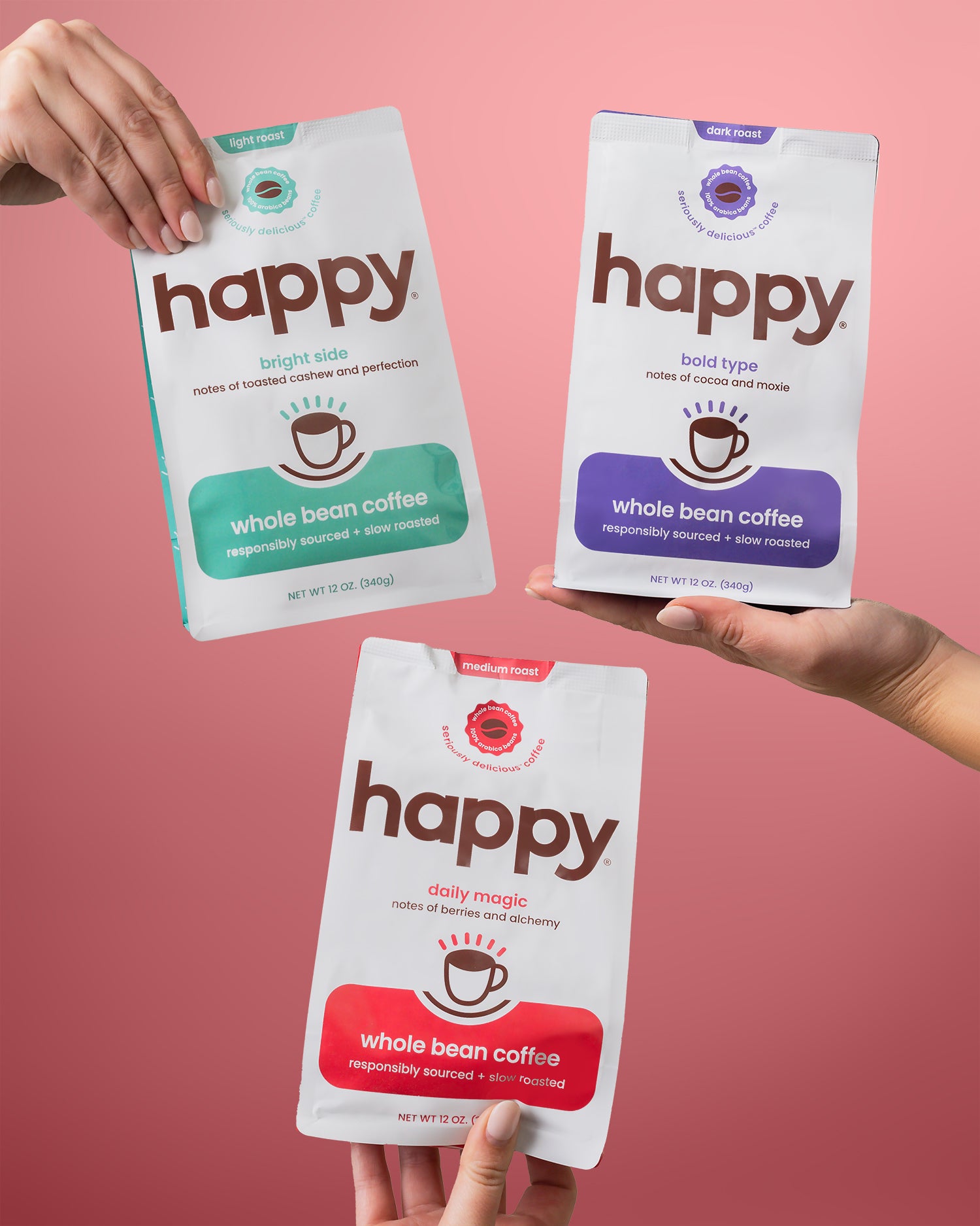 Three 'happy' whole bean coffee packages held by hands against a pink background