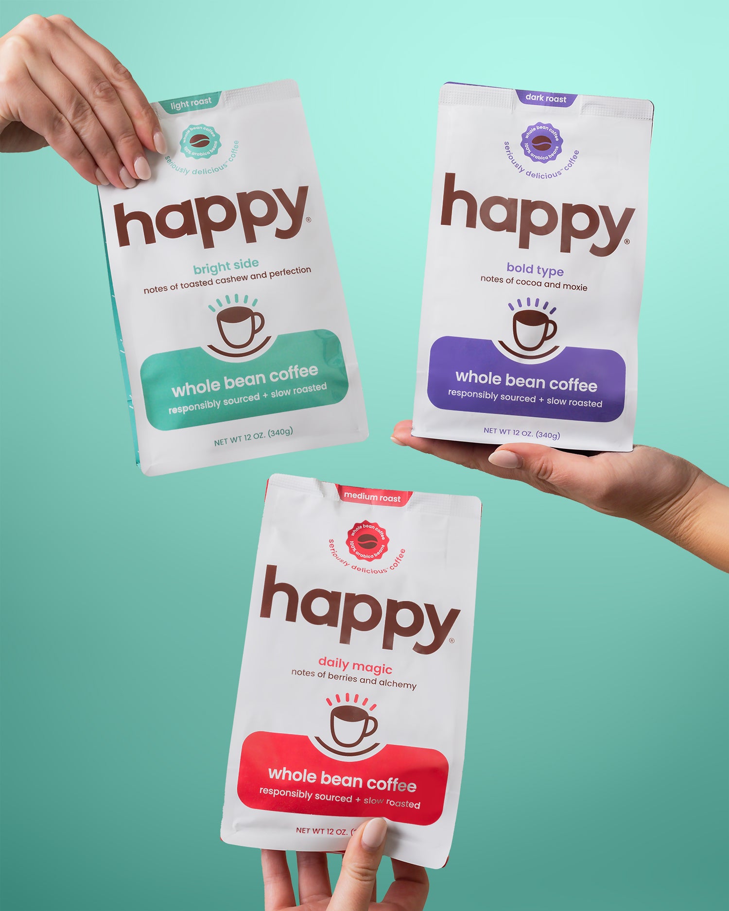 Three packages of 'happy' whole bean coffee held by hands against a teal background