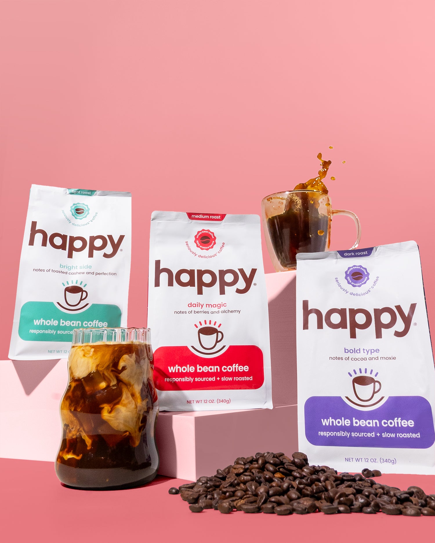 Three packages of 'happy' whole bean coffee with iced coffee and coffee beans on a pink background