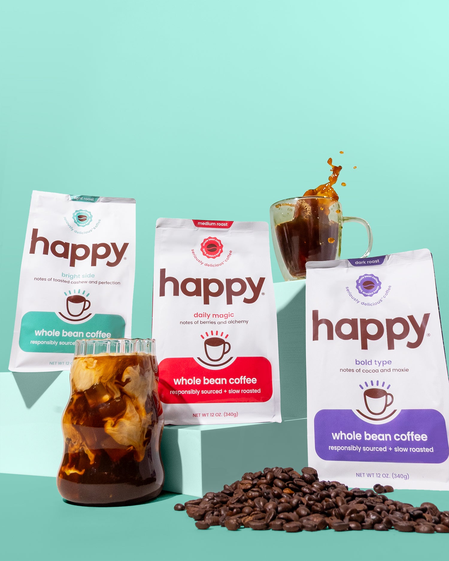 Three packages of 'happy' whole bean coffee with a glass of iced coffee and coffee beans on a teal background.