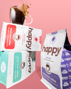 Three 'happy' brand coffee packages on a pink background with a cup of coffee.