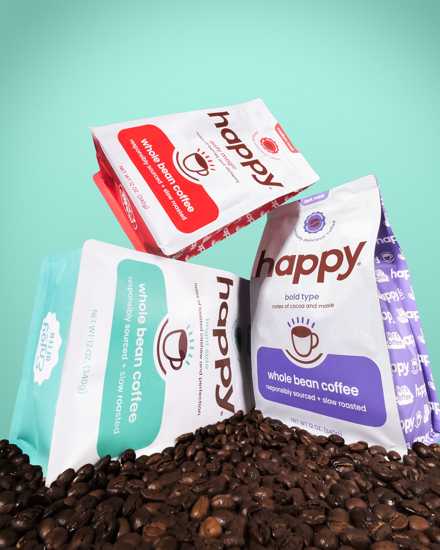 Three packages of 'happy' whole bean coffee on a bed of coffee beans with a teal background.