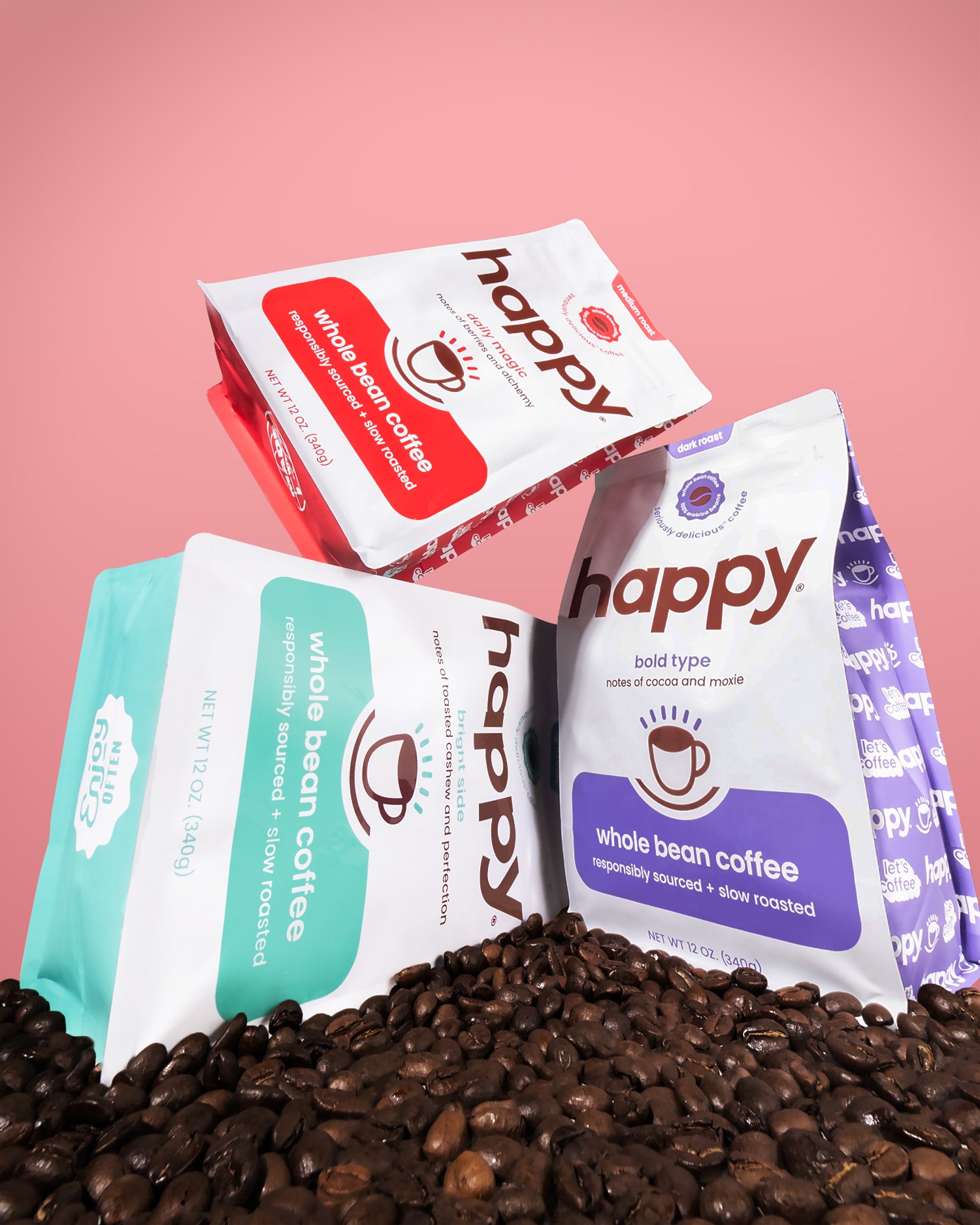 Three 'happy' brand coffee packages on a bed of coffee beans with a pink background