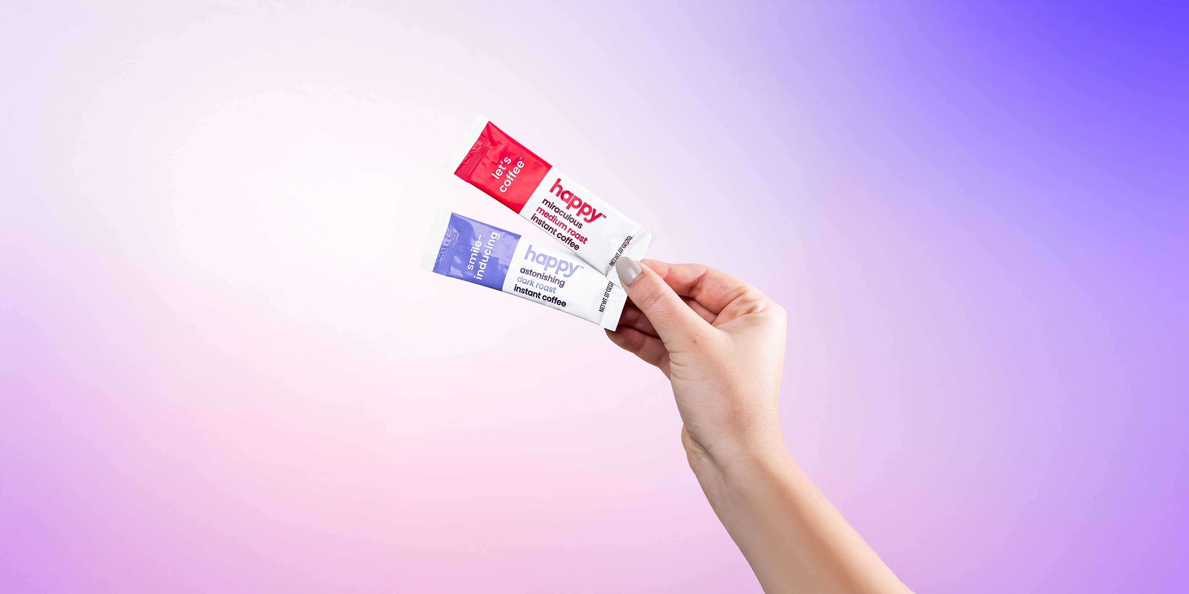 Hand holding a set of colorful instant coffee sachets against a gradient background