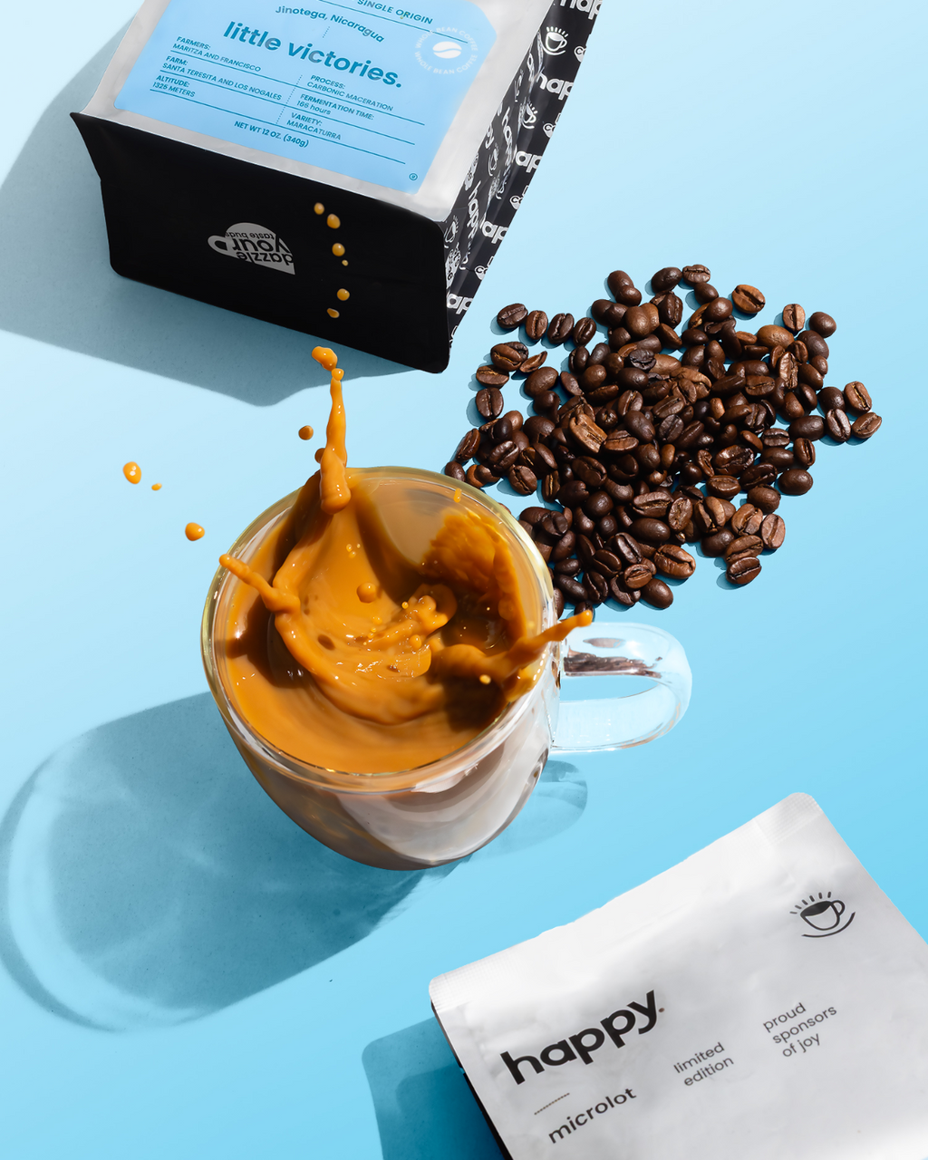 Glass mug with coffee, coffee beans, and a bag of 'happy Little Victories' high quality specialty coffee on a blue background