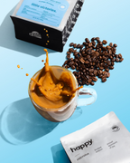 Glass mug with coffee, coffee beans, and a bag of 'happy Little Victories' high quality specialty coffee on a blue background