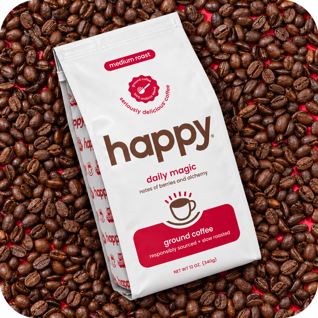 A bag of Happy Daily Magic medium roast ground coffee placed diagonally on a bed of whole coffee beans. The white bag features brown and red branding, and the background is completely covered with roasted coffee beans.