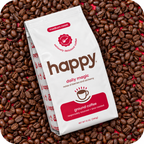 A bag of Happy Daily Magic medium roast ground coffee placed diagonally on a bed of whole coffee beans. The white bag features brown and red branding, and the background is completely covered with roasted coffee beans.
