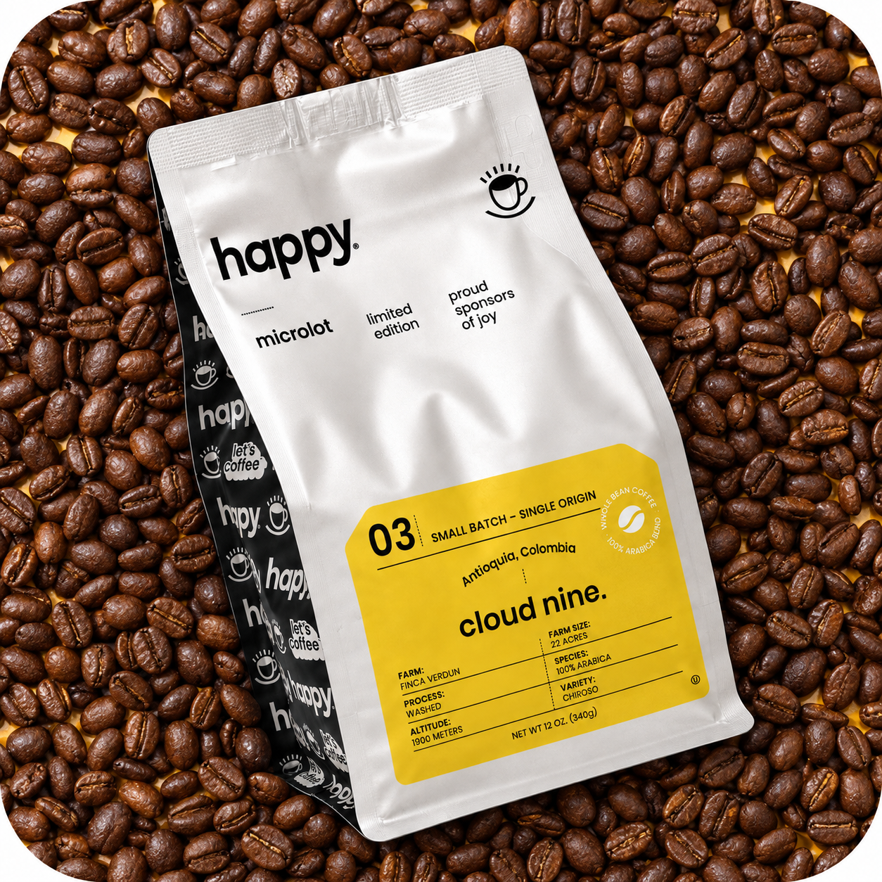 A bag of Happy Microlot Cloud Nine coffee beans lies on top of a dense bed of roasted coffee beans. The bag is white with a bright yellow label on the lower right and black text/logo.