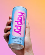 Hand holding a blue can of 'happy' tahitian vanilla cold brew coffee with pink label against a gradient background