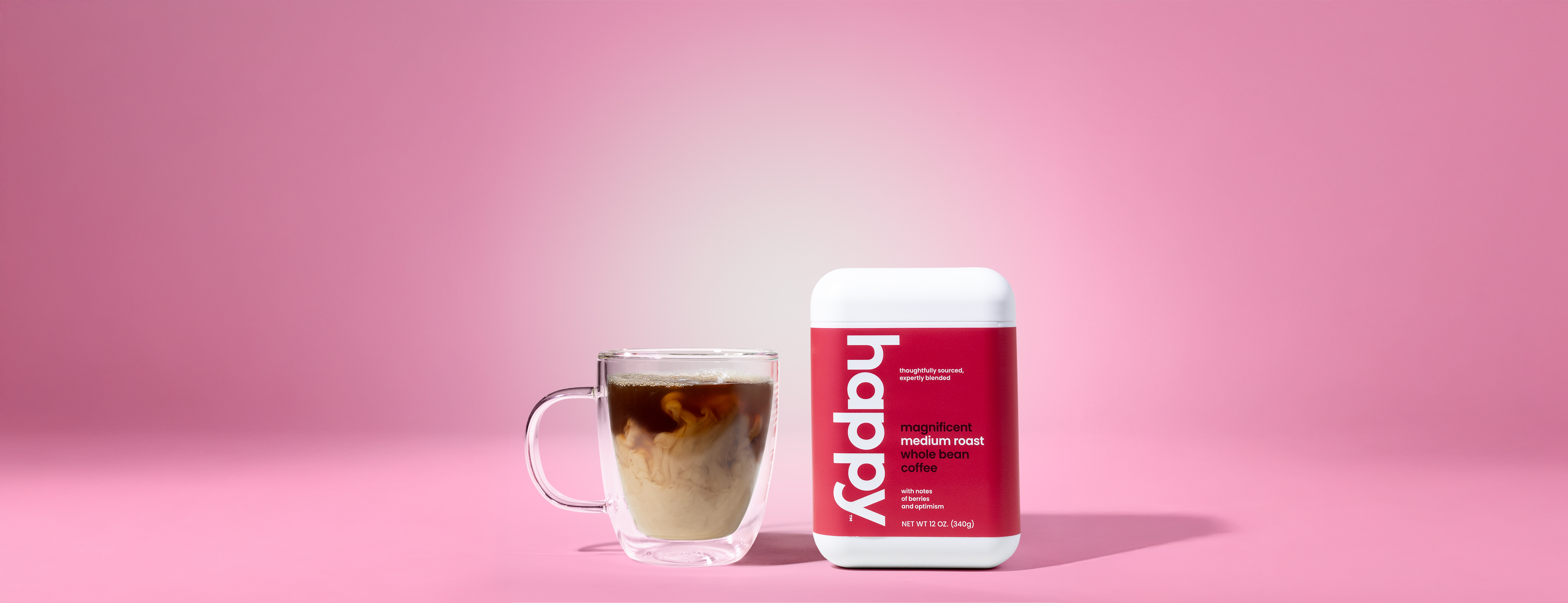 Magnificient Medium Roast Whole Bean Coffee container with a glass of iced coffee on a pink background